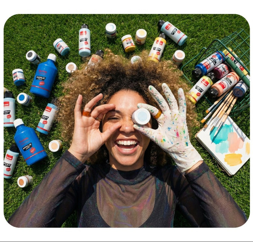 Smiling painter lying on the grass surrounded by Brushible paint bottles